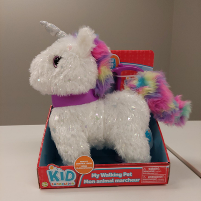 White unicorn plush toy with a silver horn and rainbow tail in its box.