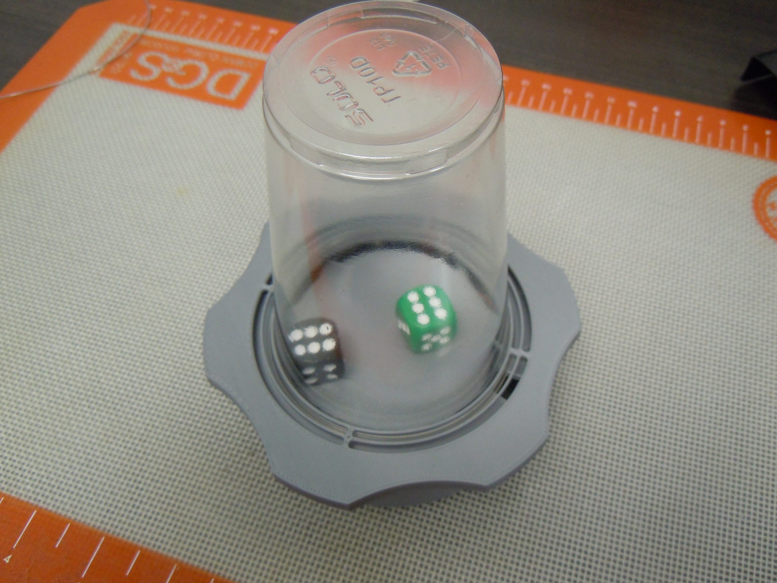 Top view of a grey 3d printed dice roller with a transparent plastic cup as a lid. Inside is a green and black dice.