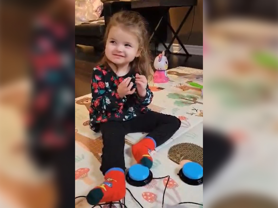 A young girl sitting on the floor using her feet to activate an assisistive switch.