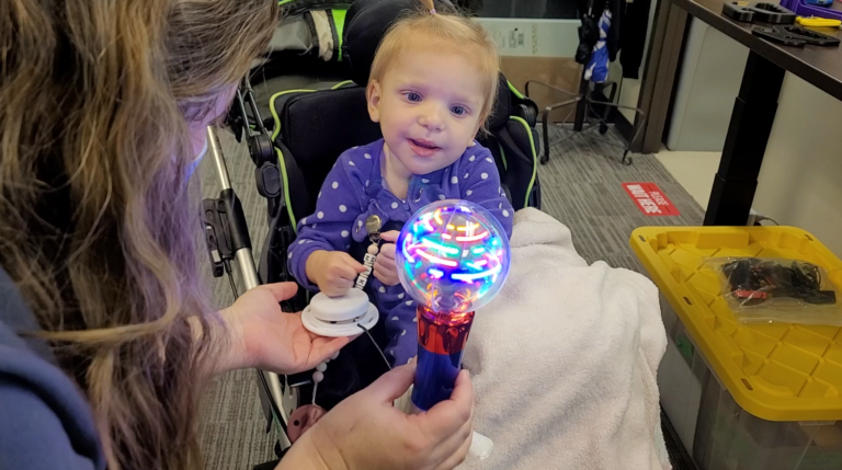 A child looking at a spinning light wand being activated by an assistive switch.
