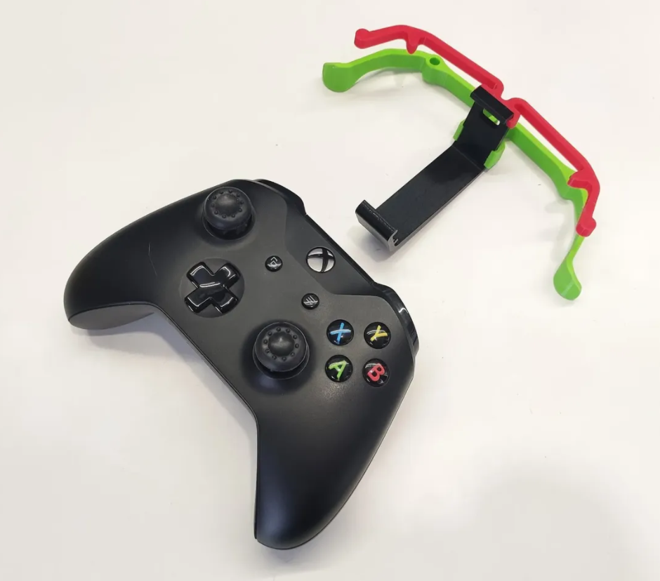 A black Xbox One controller with a green and red 3d printed trigger and button extender beside it.