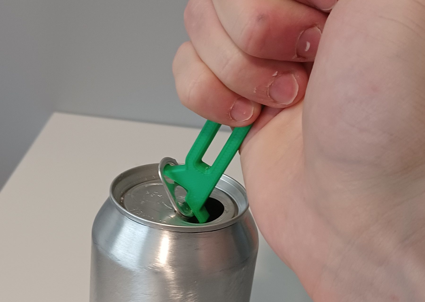 A hand using a green 3d printed beverage can opener to open a soda can.
