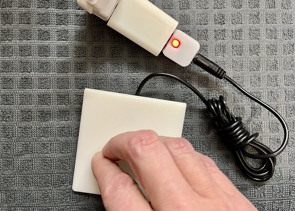 A hand pressing on a white assistive switch that's plugged into the USB Switch tester.