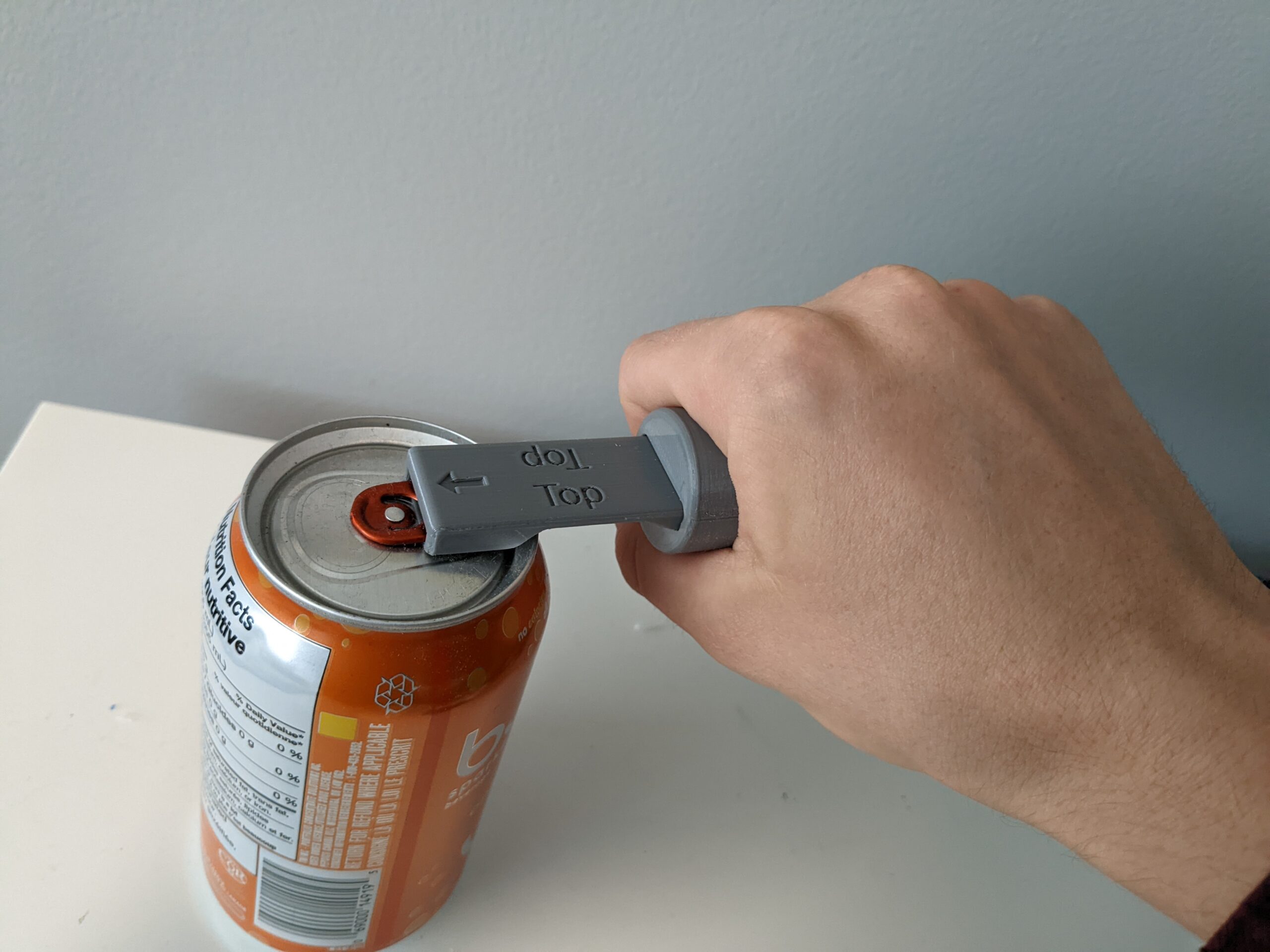 A hand holding a 3D printed can opener with cylindrical handle to open a pop can.