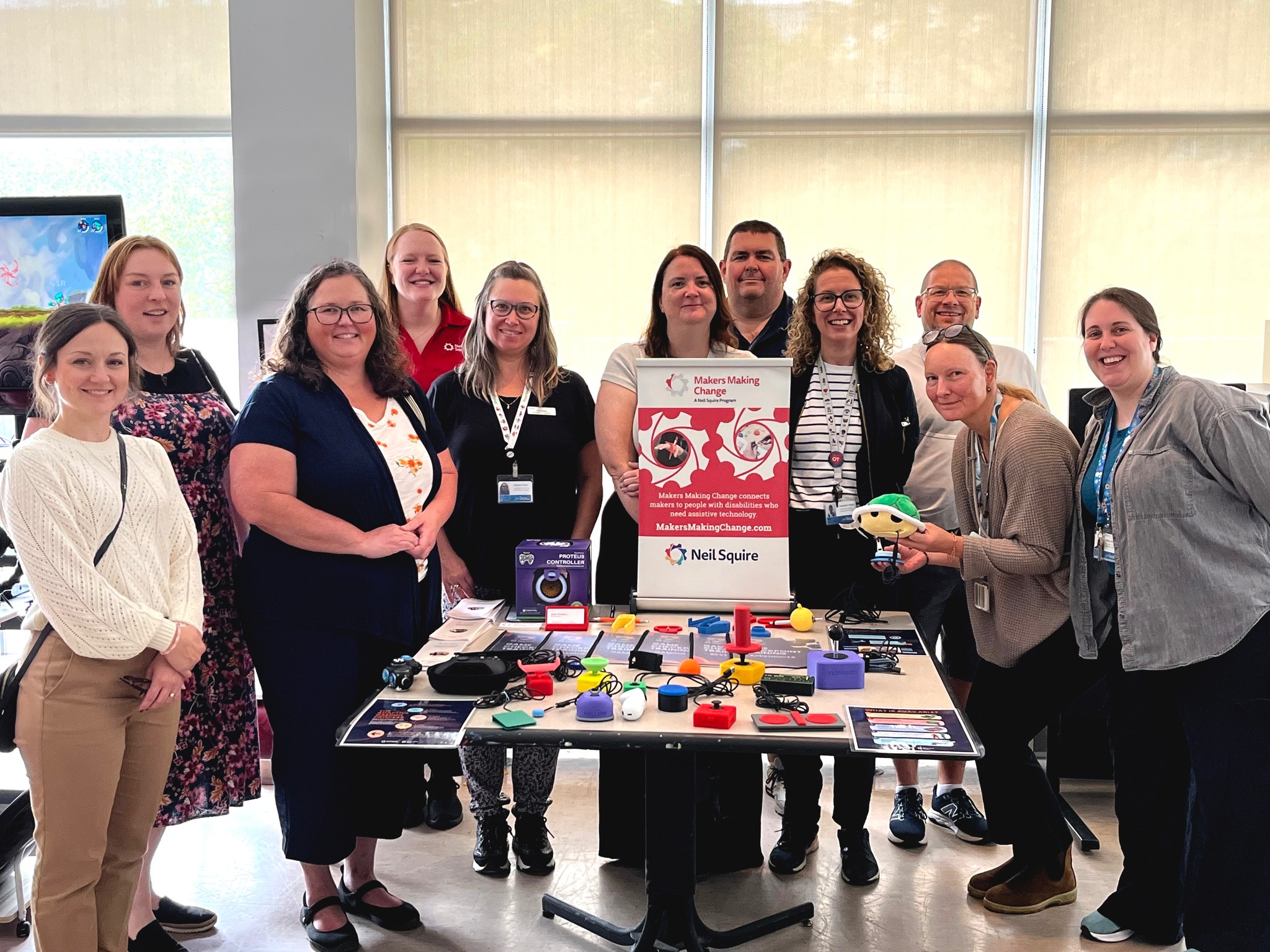 Clinicians at the Nova Scotia Rehabilitation and Arthritis Centre and MMC staff pose together for a photo next to a table with an MMC banner and adaptive gaming devices.