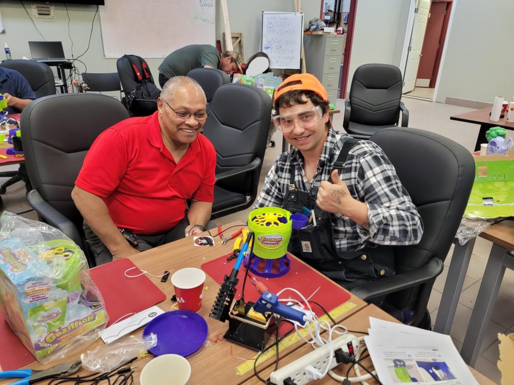 Two participants smiling and doing a thumbs up beside their built adapted toy.