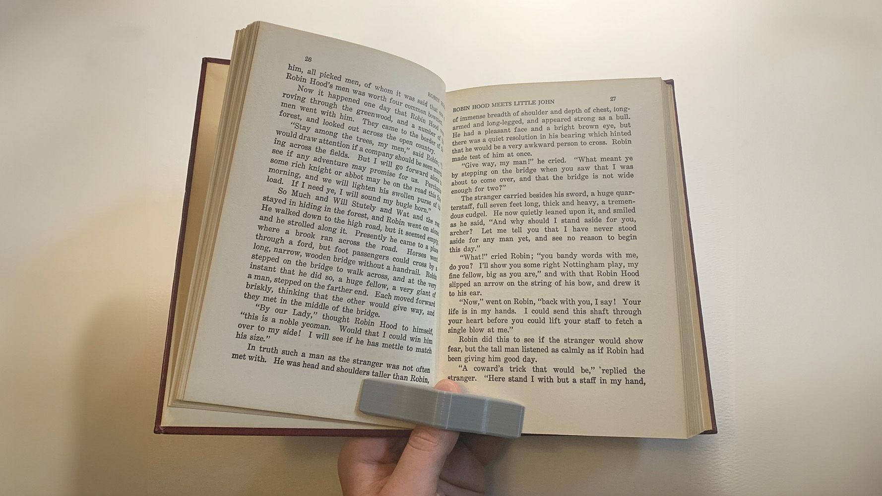Person using book holder device to hold open pages of a book with one hand