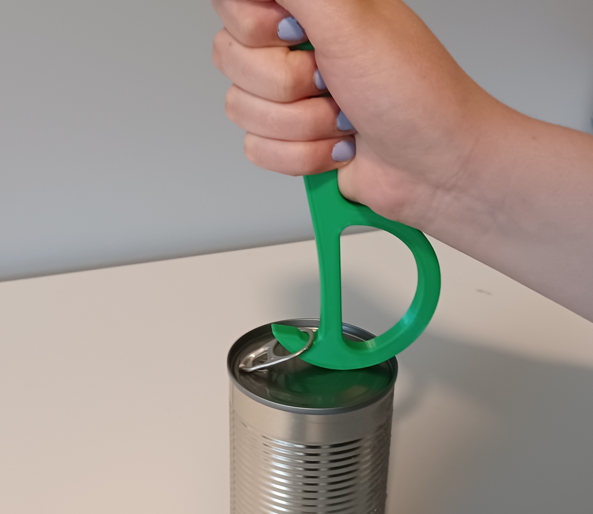 Hand hooks the Pull-Tab Tin Can Opener around the pull-tab of a can.