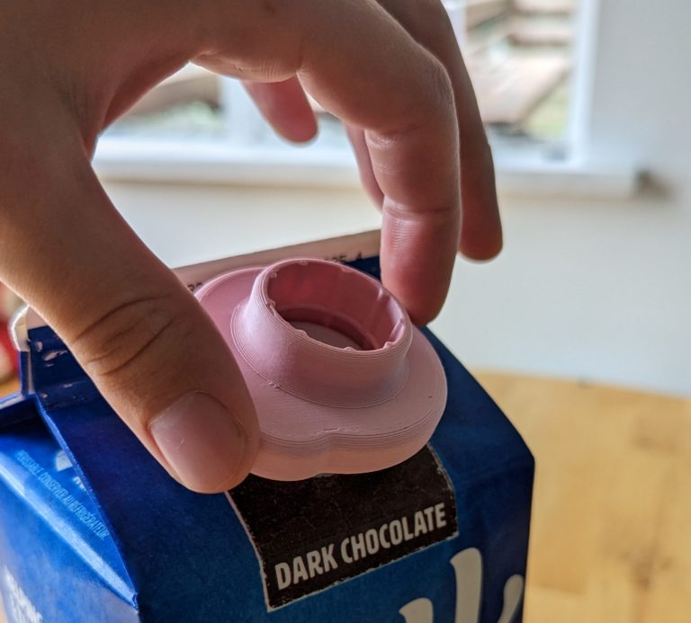 A pink milk carton opener being used to open a carton of Silk soy milk.