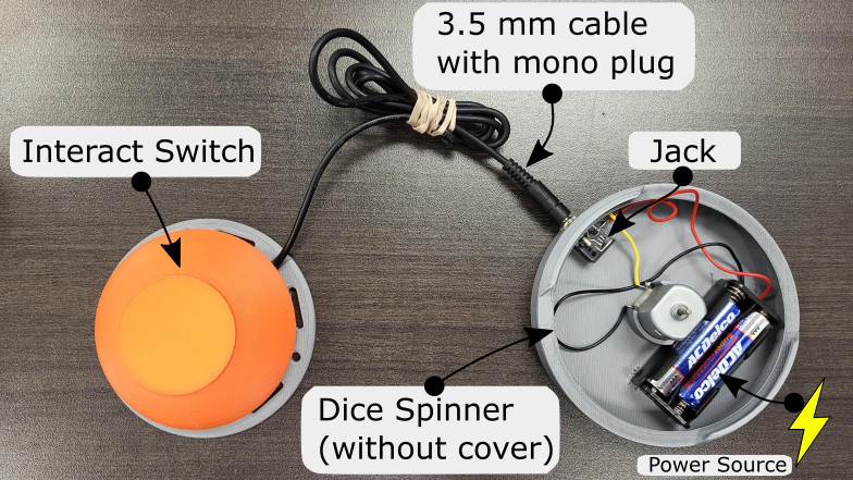 An orange Interact Switch attached to an adapted Dice Spinner using a 3.5 mm cable with mono plug.