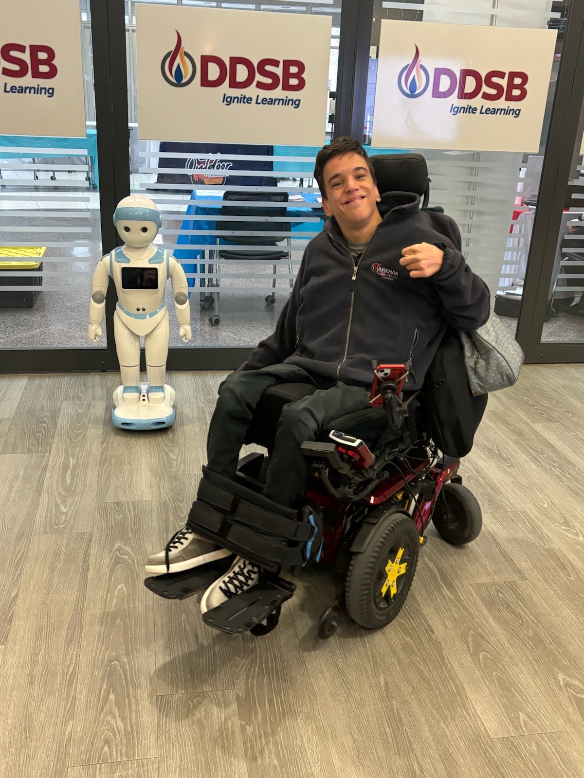 Nico in a wheelchair, in front of signs for the Durham District School Board.