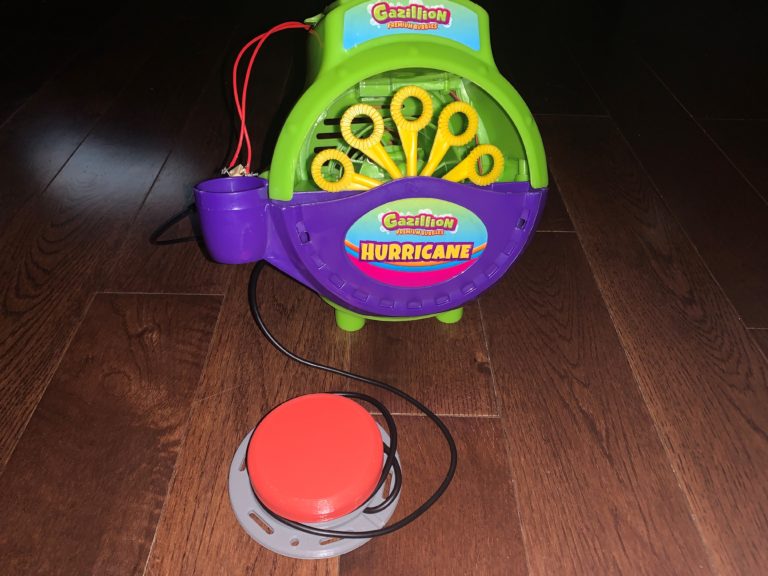 A switch-adapted bubble blower connected to a red assistive switch.