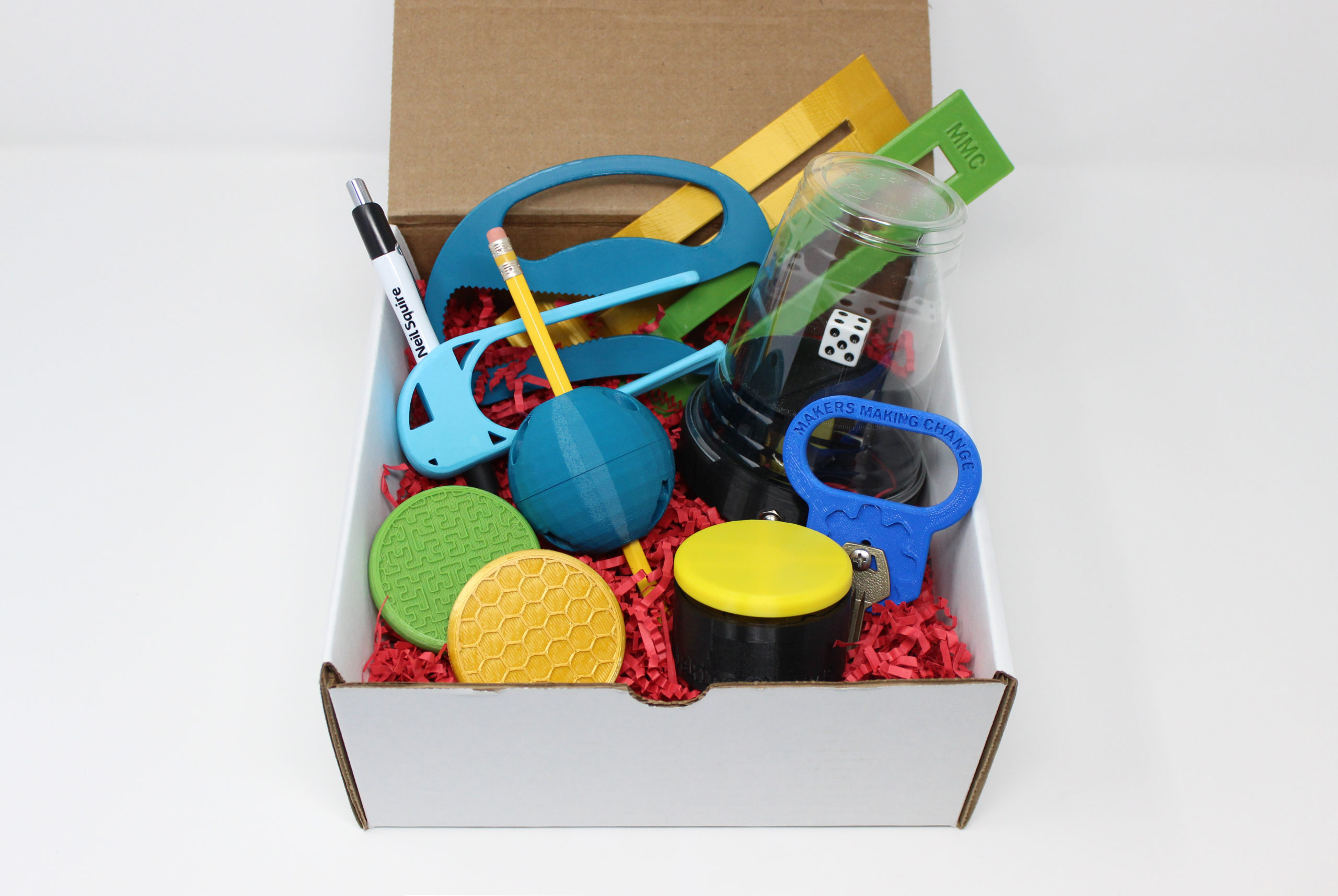 A box with 3d printed assistive devices like dyslexia reading bar, bottle opener, writing aids, dice spinner, key turner, and access switch