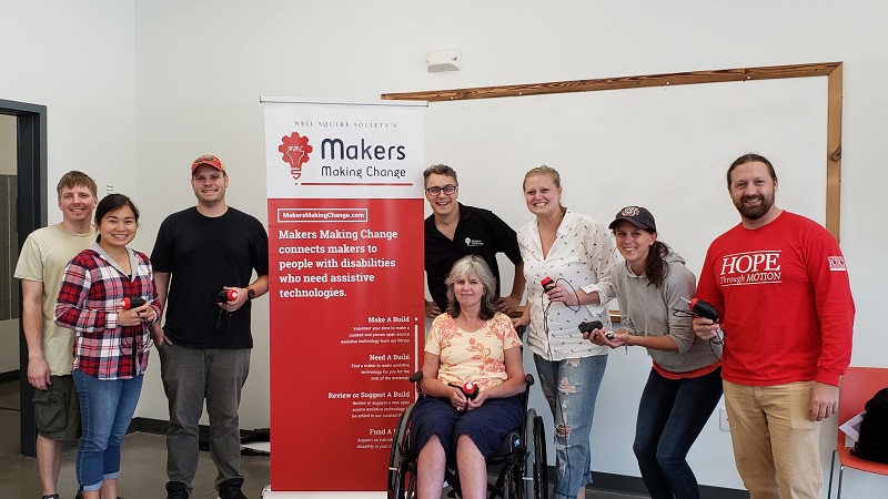 Makers at the Kennedy Krieger Institute with their built devices and a Makers Making Change banner.