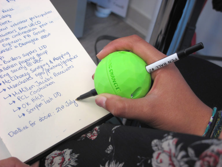 A hand using a neon green Pen Ball to write.