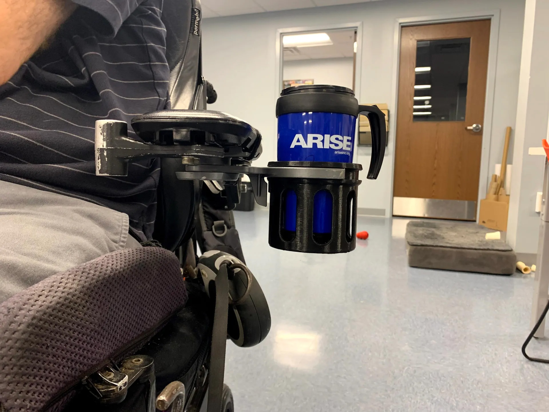 A 3d printd cup holder attached to a wheelchair holding a blue tumbler.