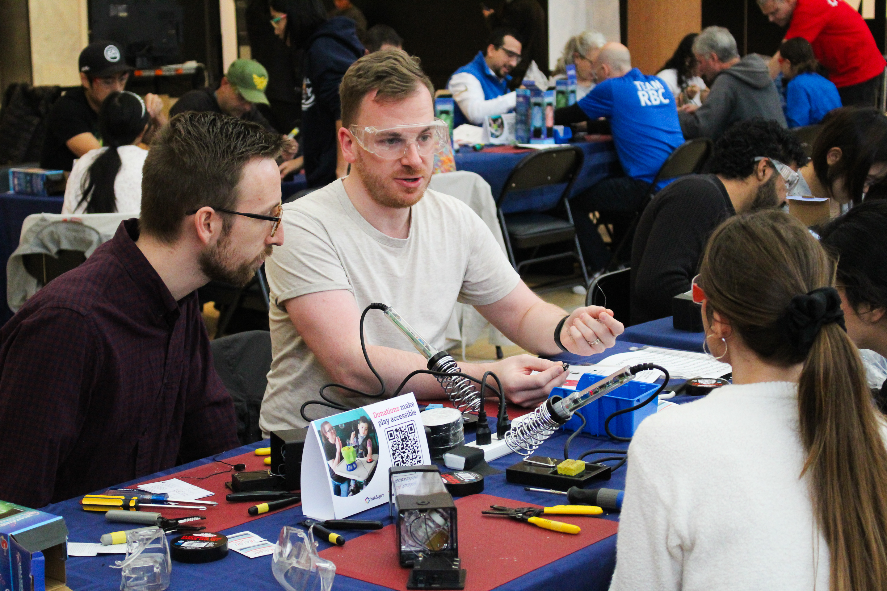 A man wearing safety talks with his fellow toy hackers.