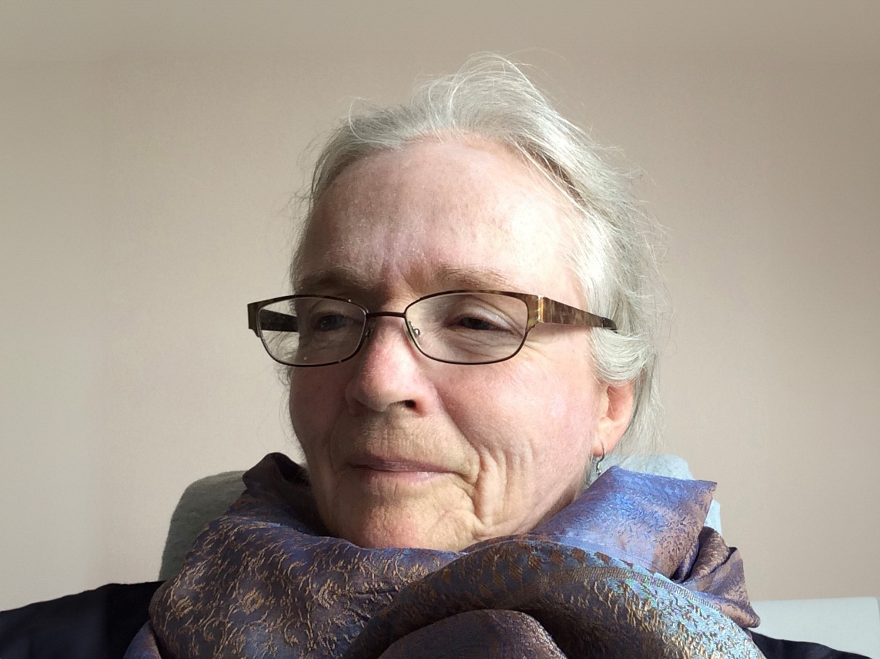 A women with white hair, gold glasses, and purple scarf.