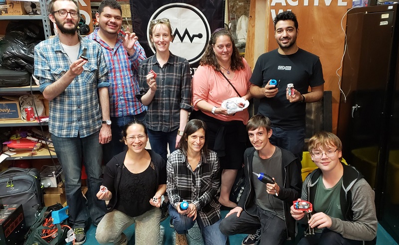 Nine makers at NYC Resistor holding their built devices.