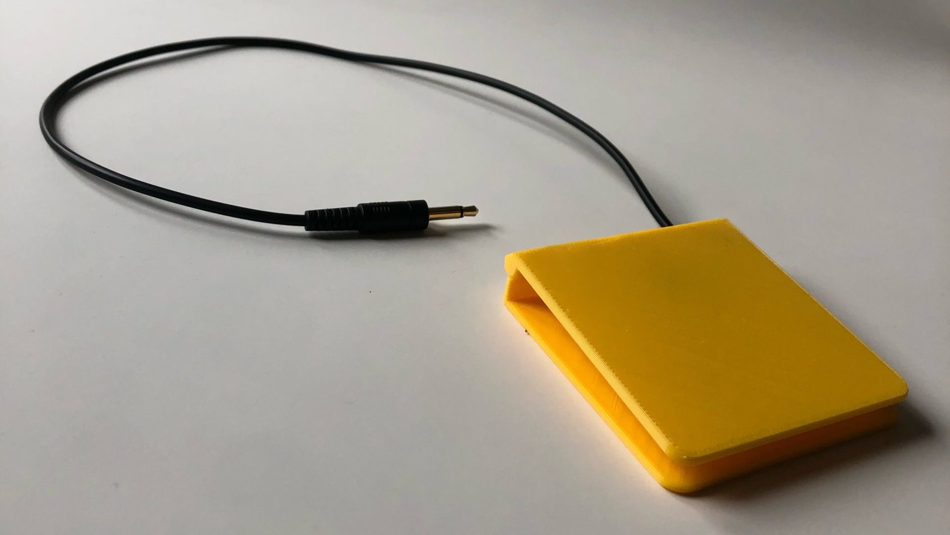 A yellow 3d printed low profile assistive switch with a mono jack end.