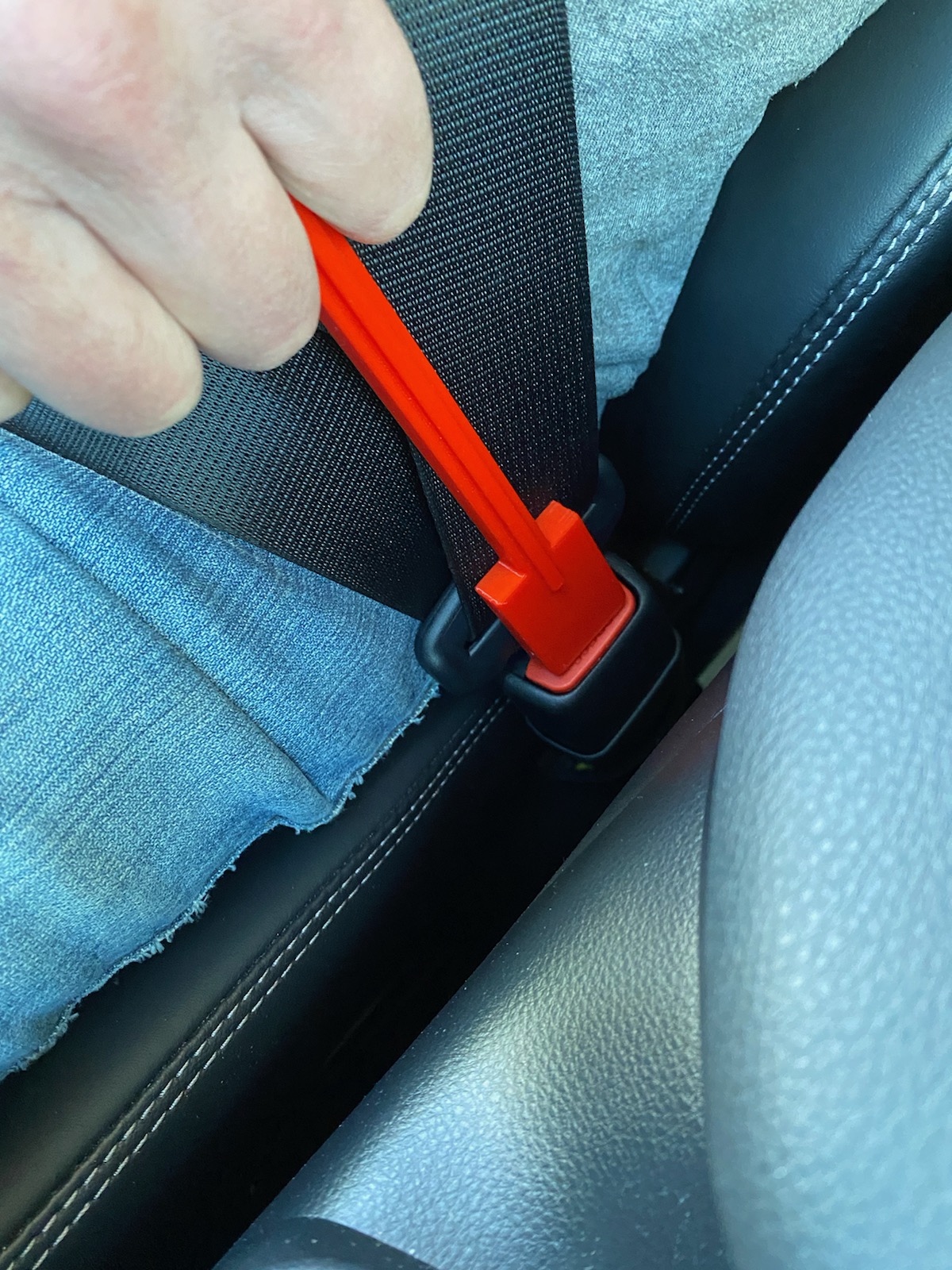 A hand holding a 3d printed seat belt pusher depressing the button on a seat belt.