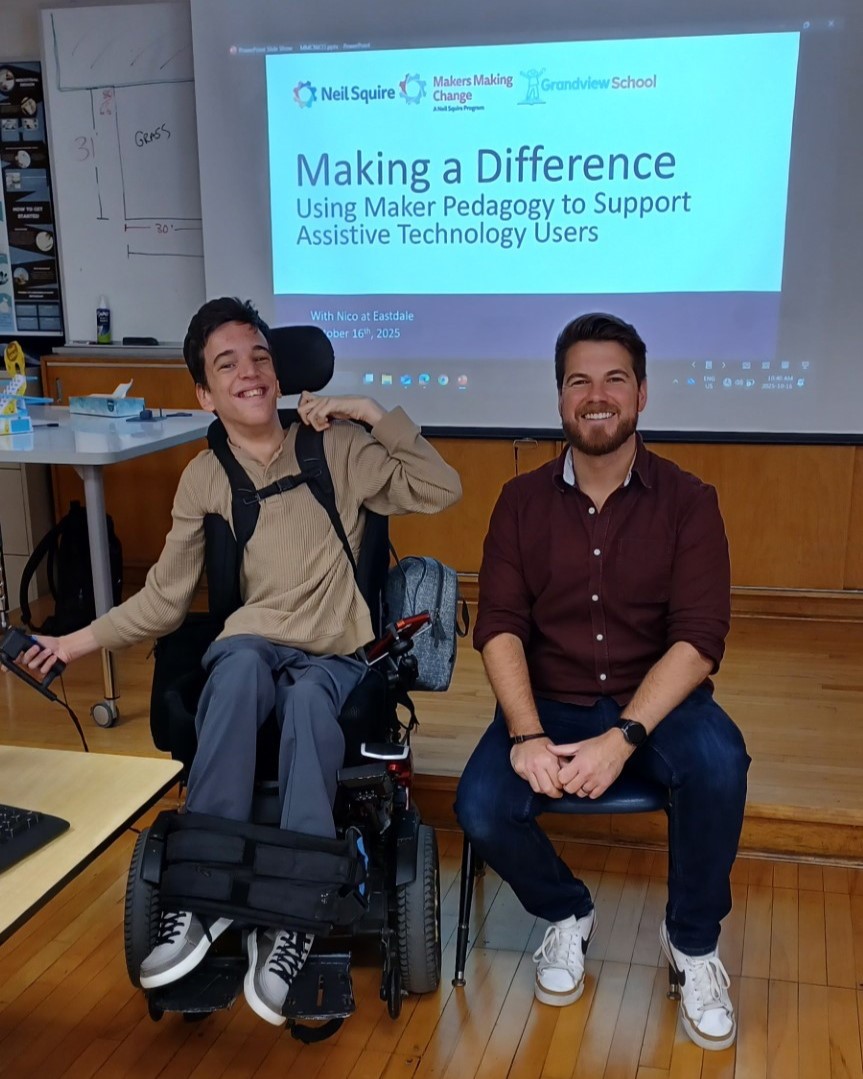 Nico, in a wheelchair, with Shaun, in front of a Makers Making Change PowerPoint presentation in a classroom.