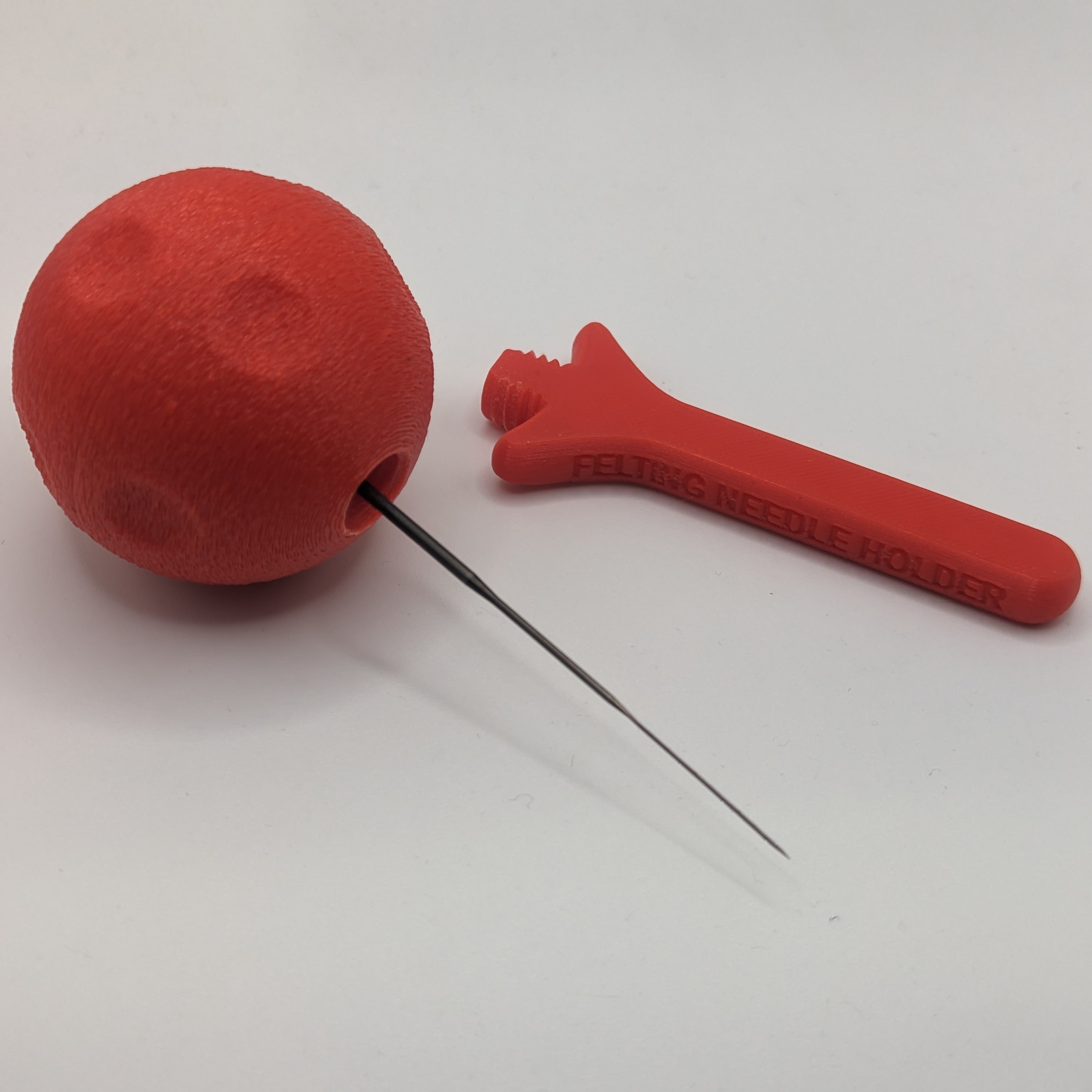 A ball-shaped Felting Needle Holder in a red filament with the cover removed.