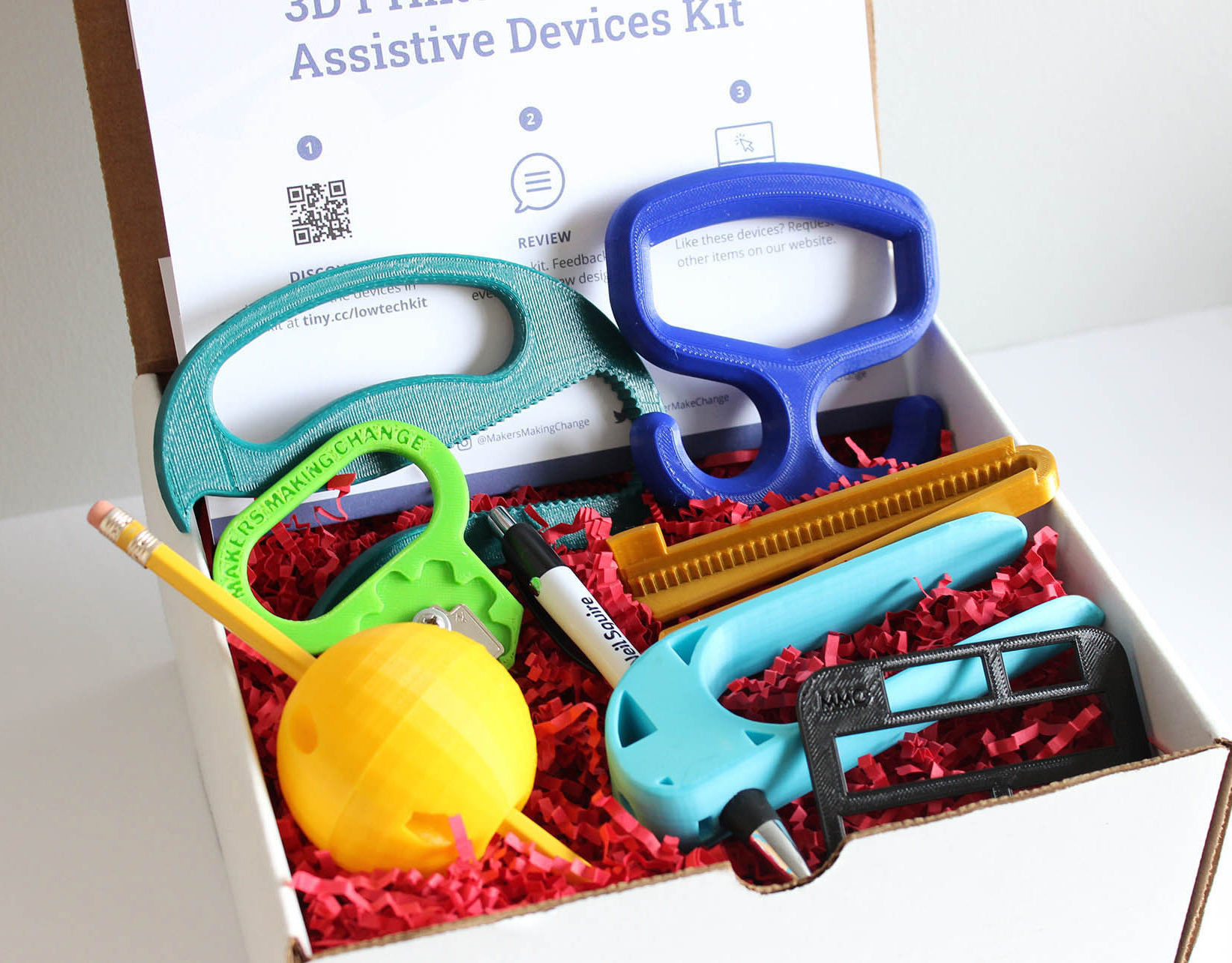 Nine 3d printed low-tech assistive devices in a white box.