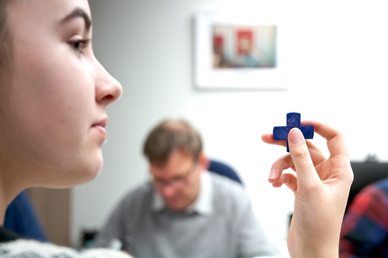 A build participant holding up a blue 3D printed part.
