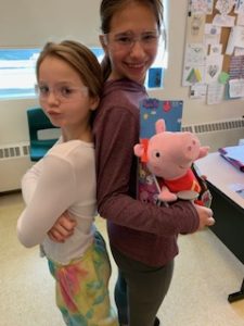 Two girls with their backs against each other holding a switch-adapted Peppa Pig.